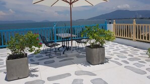 A terrace with a table and chairs, a large umbrella, and potted plants. - Santori Hotel Danang Bay (Da Nang)