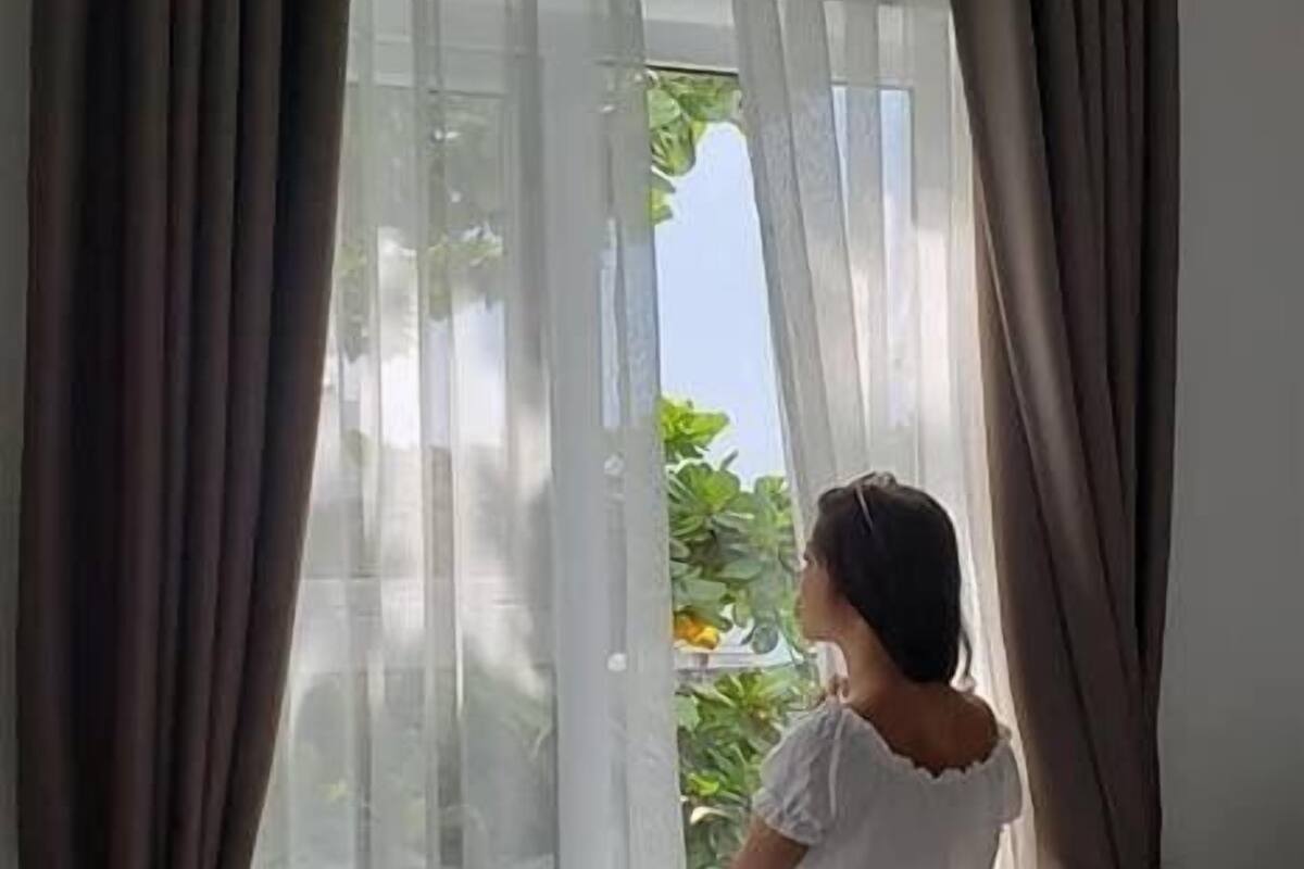 Una habitación con una cama, una ventana con cortinas translúcidas y vistas a la vegetación.