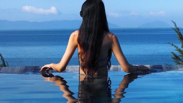 A person sitting by an infinity pool with a view of the sea and mountains. - Santori Hotel Danang Bay (Da Nang)