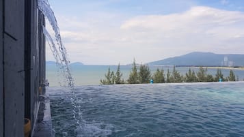Una piscina con agua que cae por la barandilla de un balcón, con vistas a una masa de agua tranquila y montañas a lo lejos.