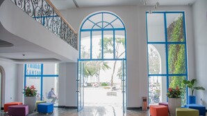 A spacious lobby with a high ceiling, a staircase with a decorative railing, and a large arched doorway leading outside. There are colorful seating areas and potted plants. - Santori Hotel Danang Bay (Da Nang)