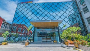 A modern building with a reflective glass facade, a prominent sign reading "Ruby Miami Hotel", and a well-maintained outdoor area with potted plants and seating. - Ruby Myanmar Hotel (Mandalay)