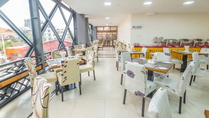 A dining area with multiple tables and chairs, a view through large windows, and a buffet setup. - Ruby Myanmar Hotel (Mandalay)
