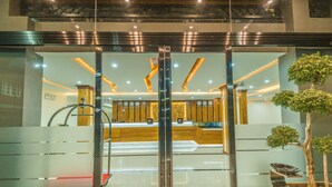 A modern hotel lobby with a glass entrance, a reception desk, and a potted plant. - Ruby Myanmar Hotel (Mandalay)