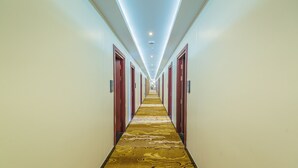 A long, narrow hotel corridor with a patterned carpet, wooden doors, and recessed lighting. - Ruby Myanmar Hotel (Mandalay)
