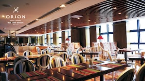 A restaurant with a modern interior, featuring wooden ceiling panels, large windows, and a variety of seating arrangements including tables and chairs.