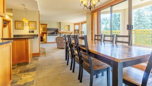 A spacious dining area with a large wooden table and chairs, a chandelier, and a view of the outdoors.