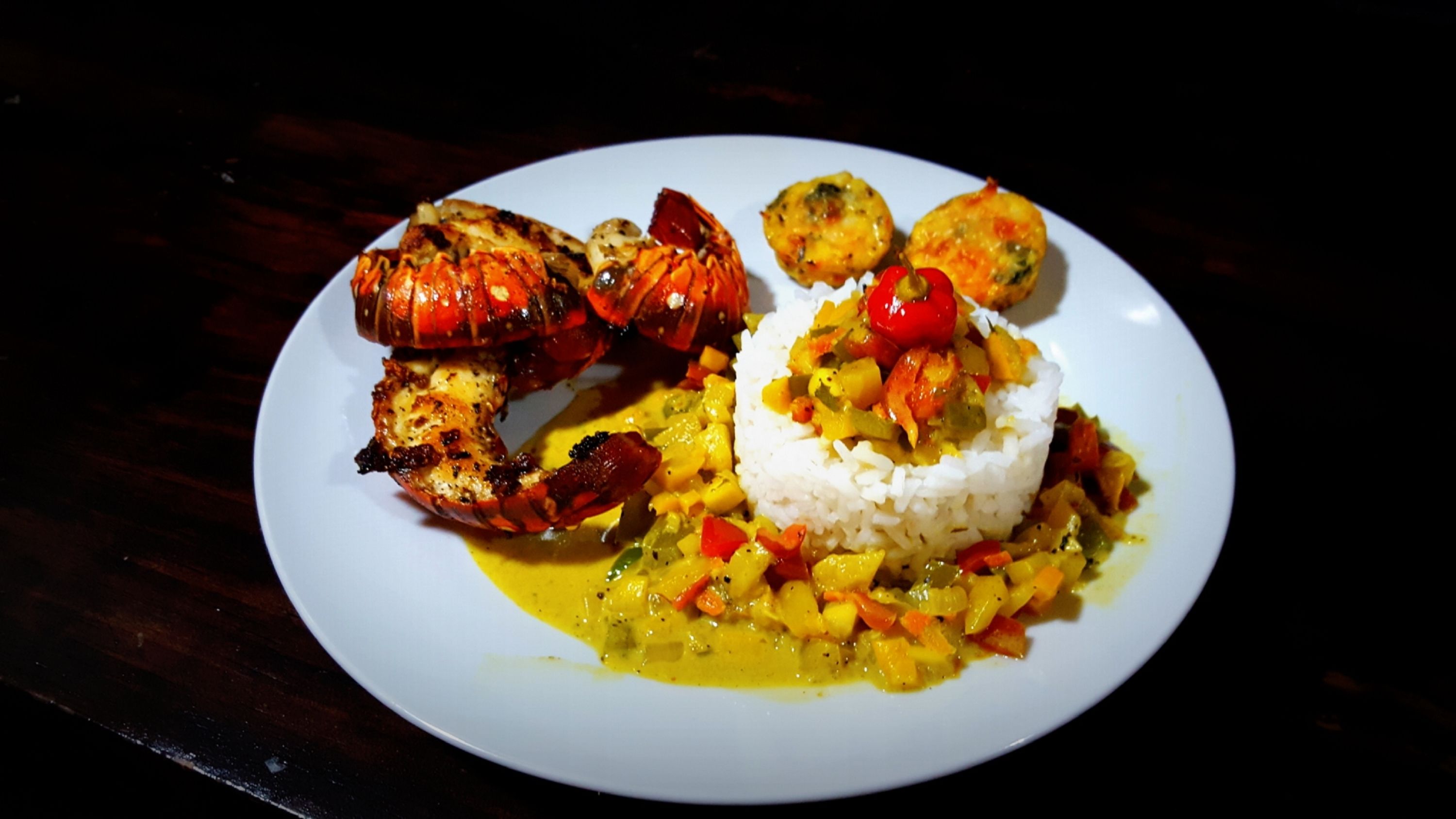 Een bord met gegrilde kreeft, witte rijst en een groentecurry.