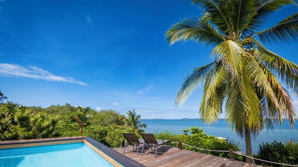 A wooden deck with a pool and lounge chairs overlooking a body of water and palm trees. - El Caribeo - Nature Lodge (Tierra Oscura)