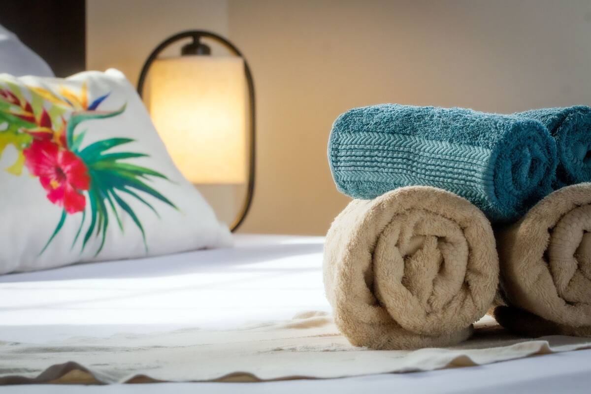 Una cama con toallas enrolladas y un cojín decorativo.