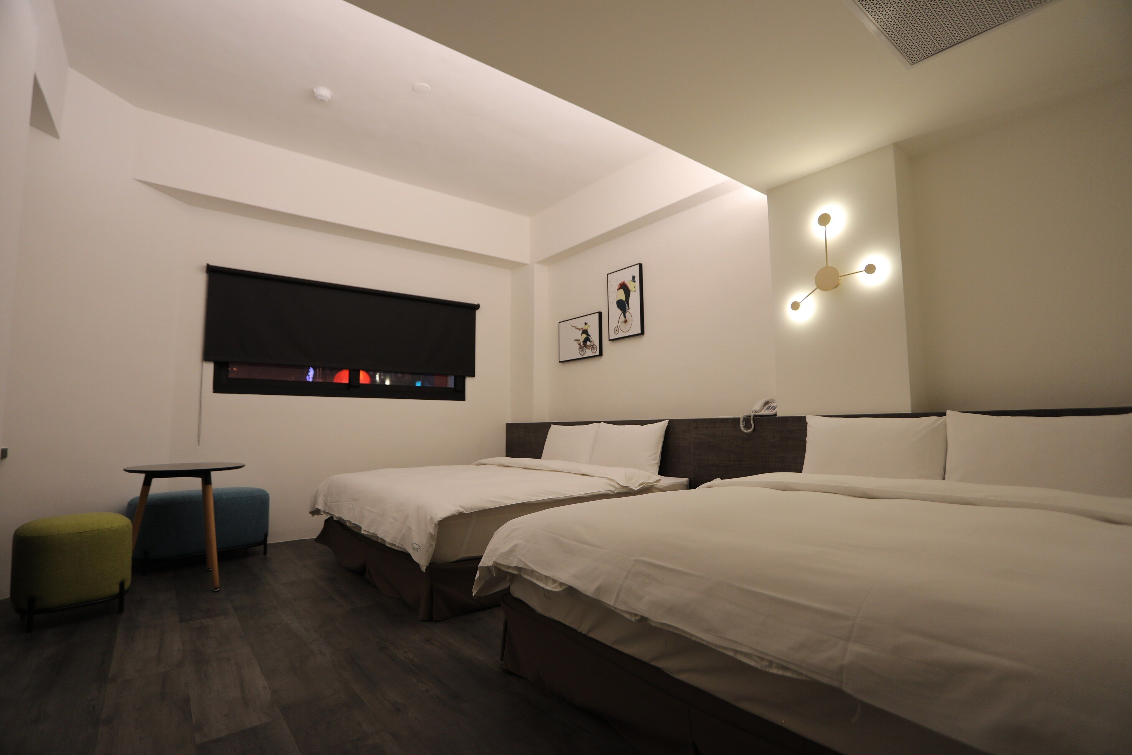A modern hotel room with two beds, a small table, and a bench.