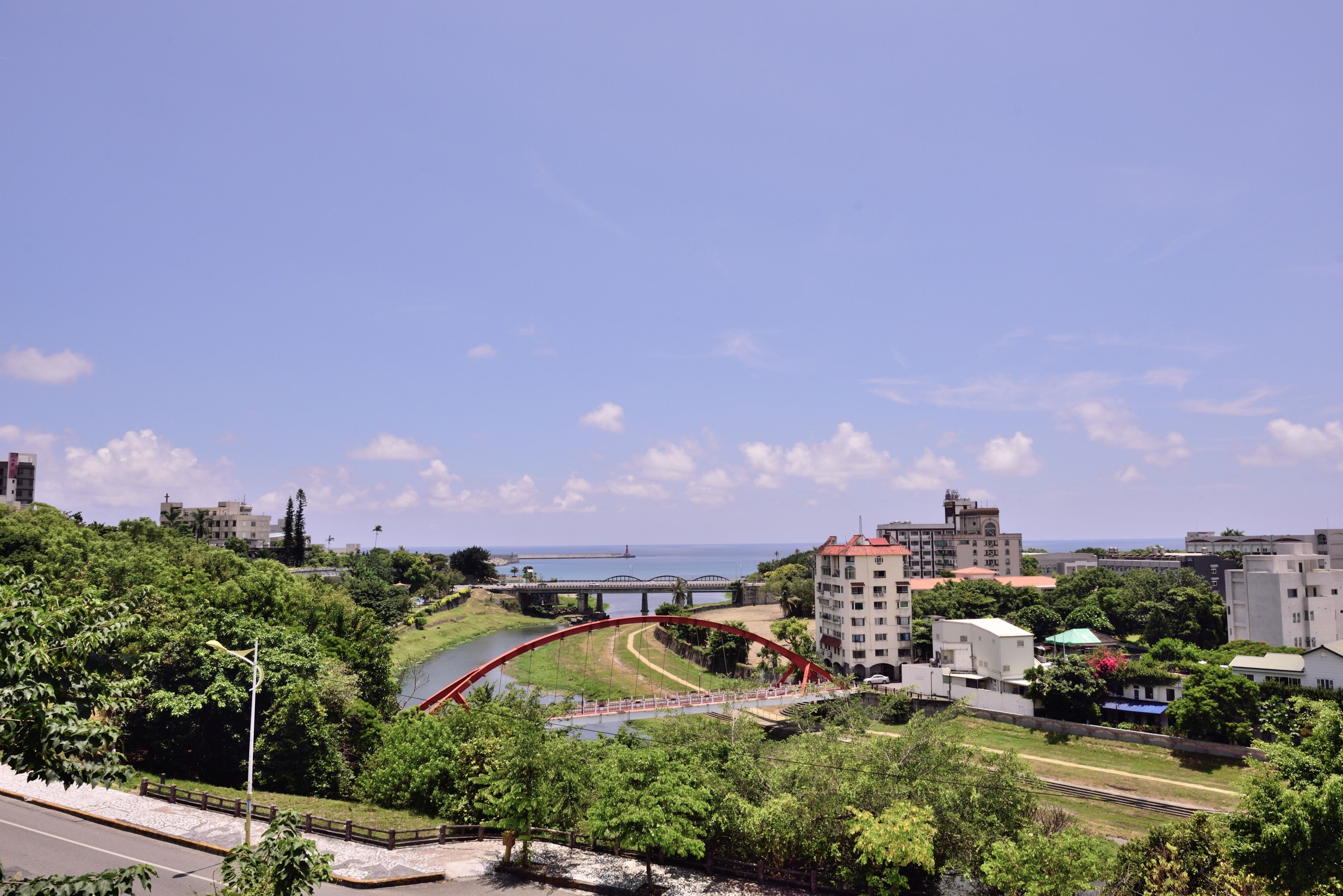 A cityscape with a prominent red bridge, lush greenery, and a body of water in the background.