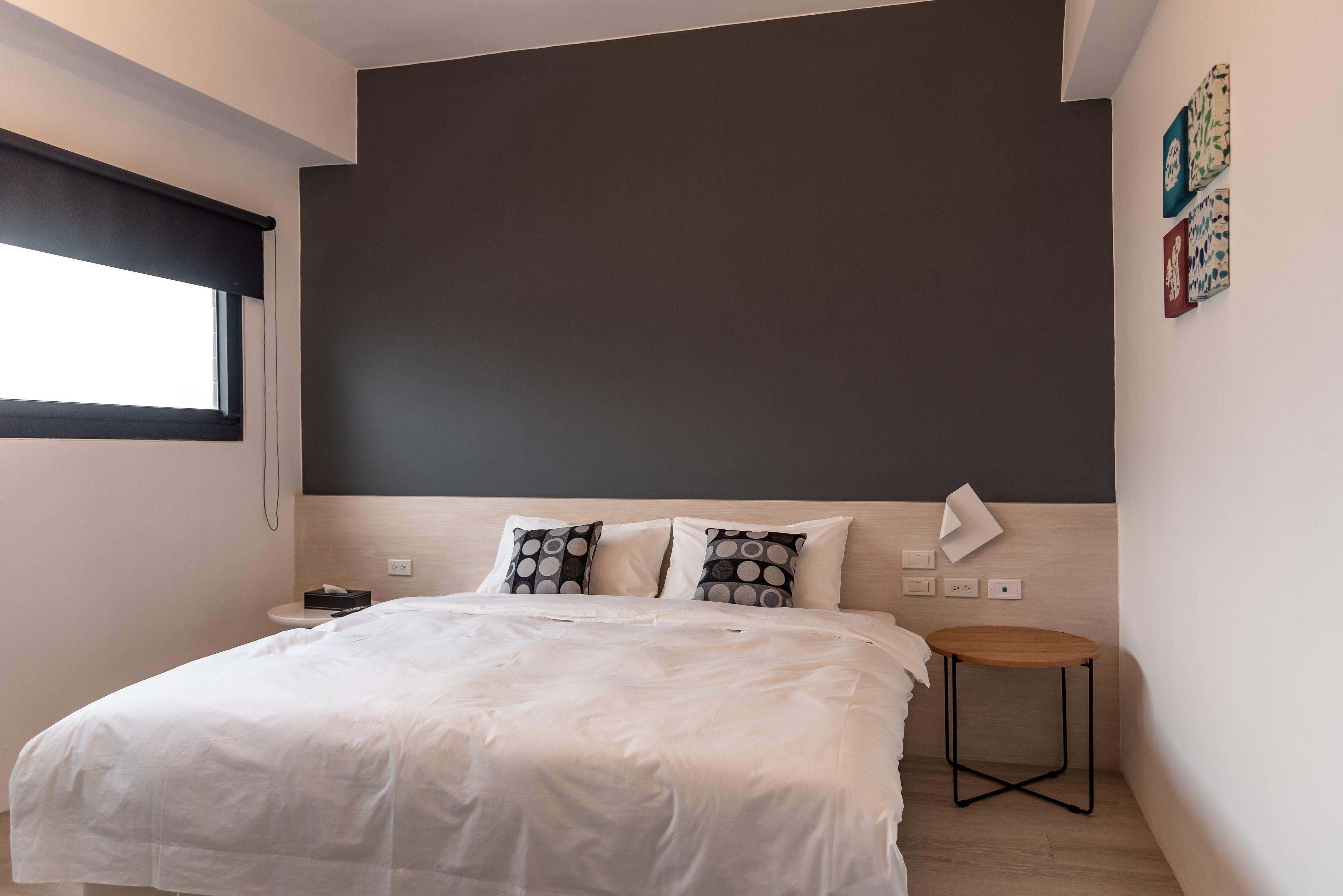 A modern bedroom with a large bed, a small bedside table, and a window with a black blind.