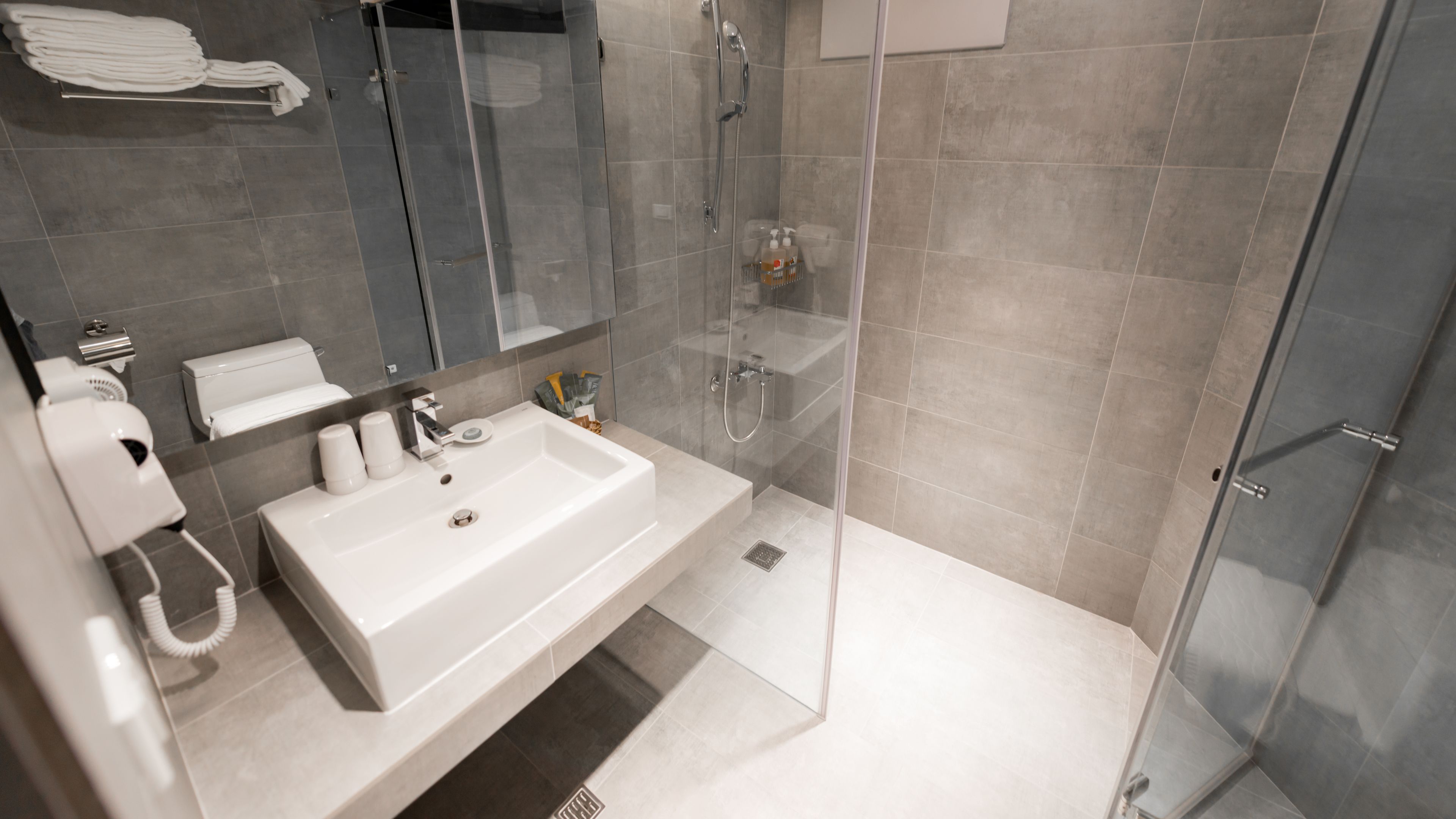 A modern bathroom with a white sink, glass shower enclosure, and grey tiles.