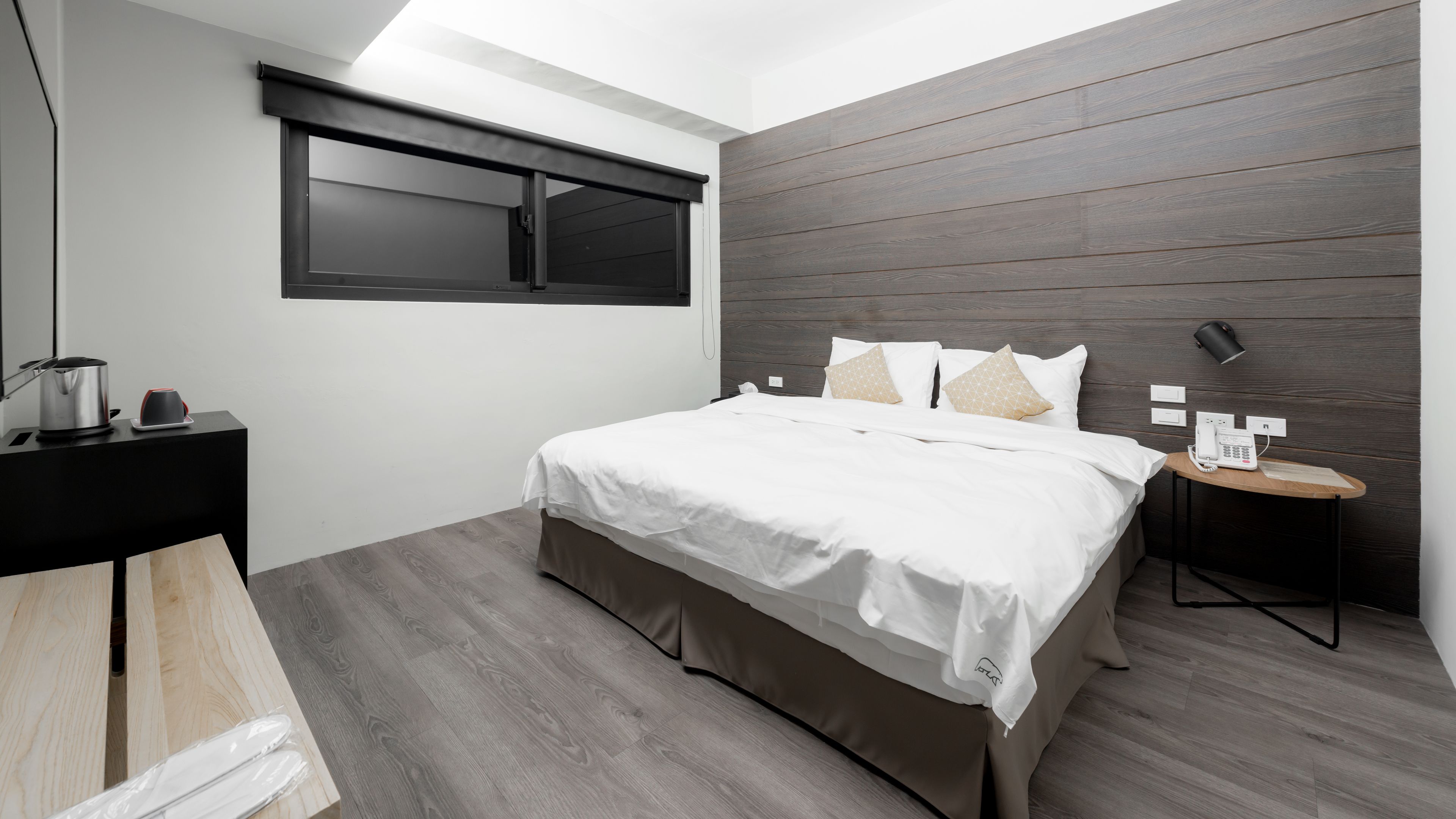 A modern bedroom with a bed, bedside table, and a small table with a phone.