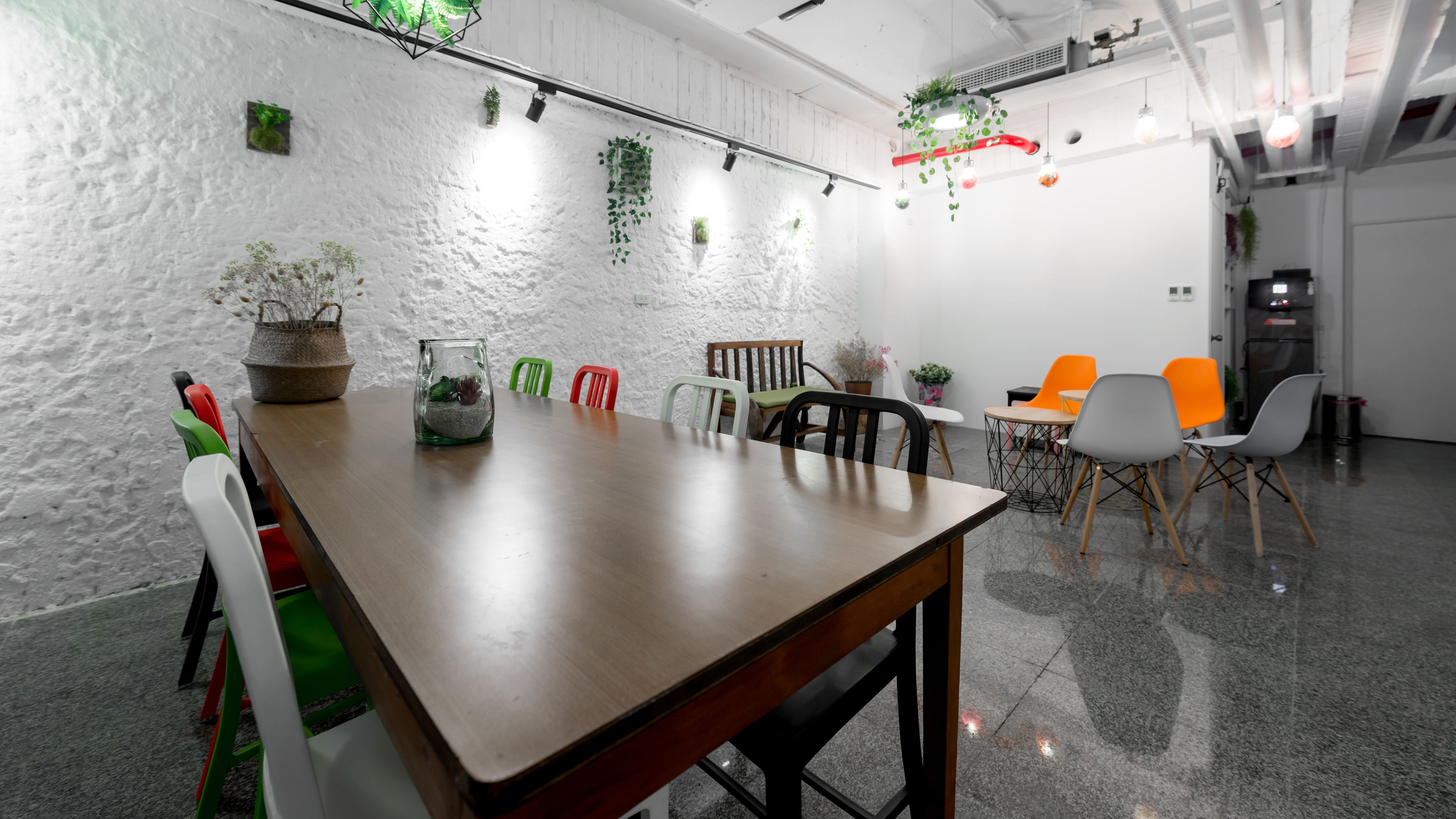 Een moderne vergaderruimte met een houten tafel, kleurrijke stoelen en groene planten aan de wit bewerkte wanden.