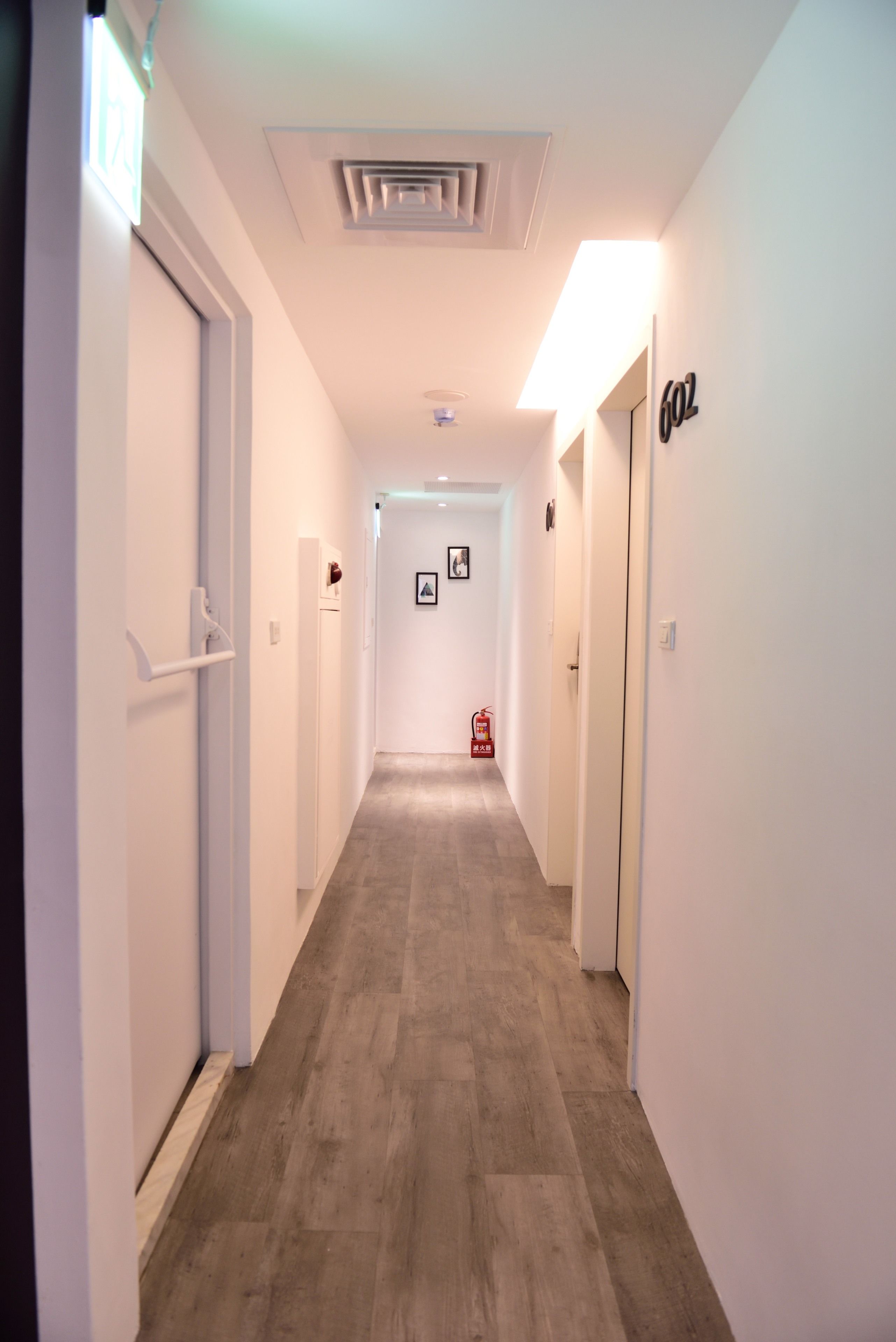 A hallway with a wooden floor, white walls, and a fire extinguisher mounted on the wall.