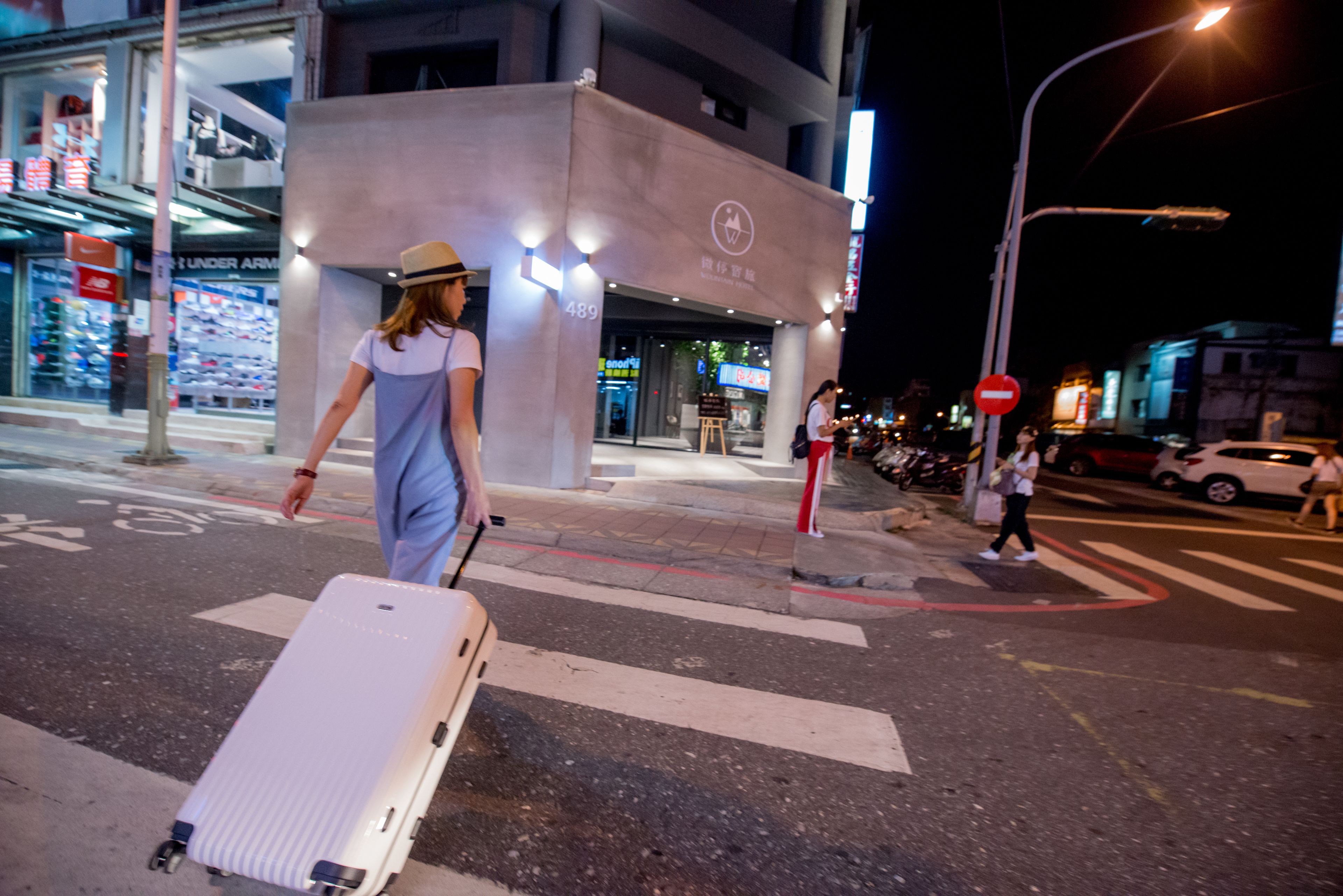 A person walking with a suitcase on a city street at night.