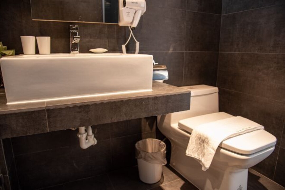 A modern bathroom with a large white sink, a toilet, and a hairdryer on the wall.