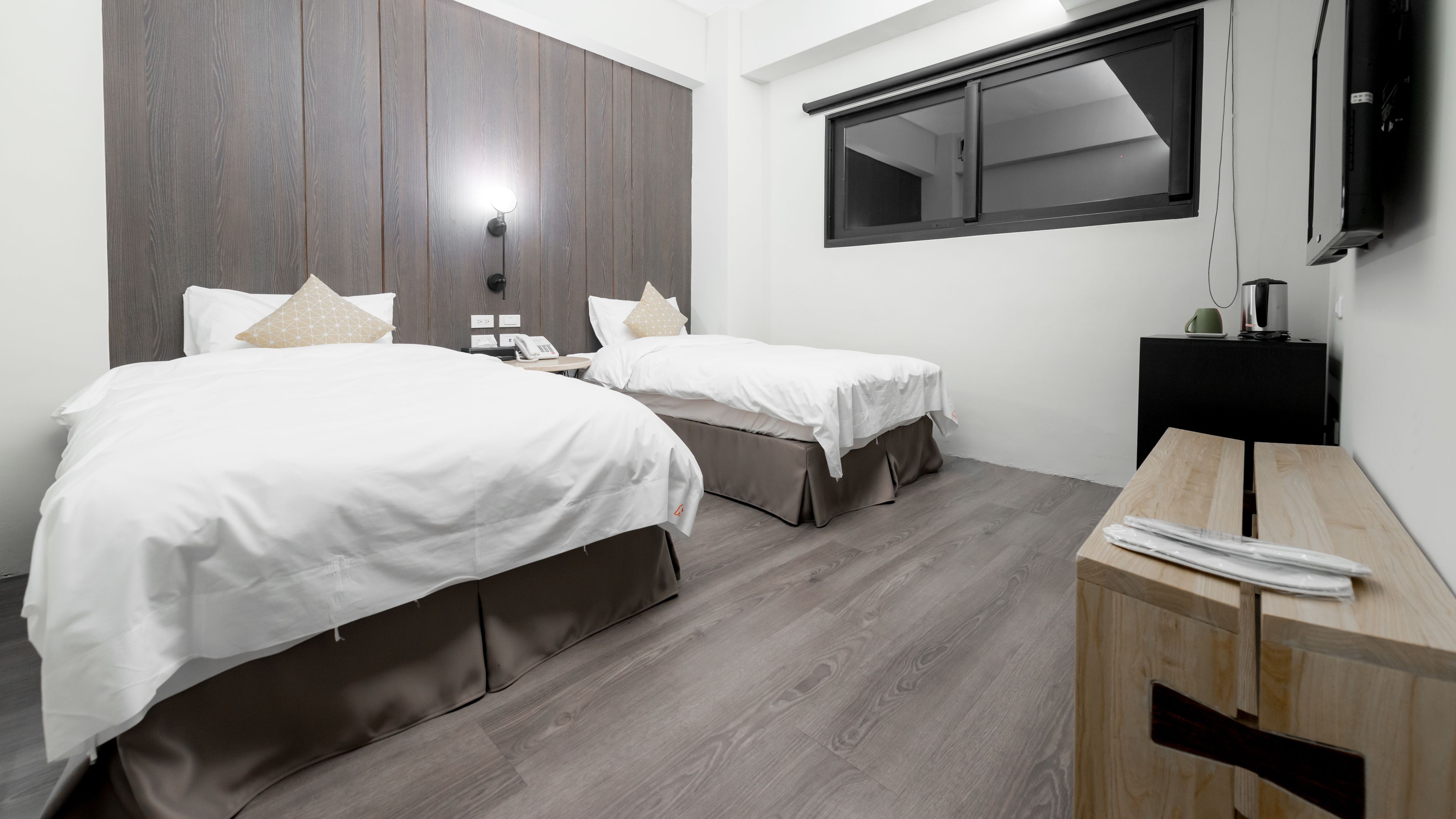 A hotel room with two beds, a wooden desk, a flat-screen TV, and a window.