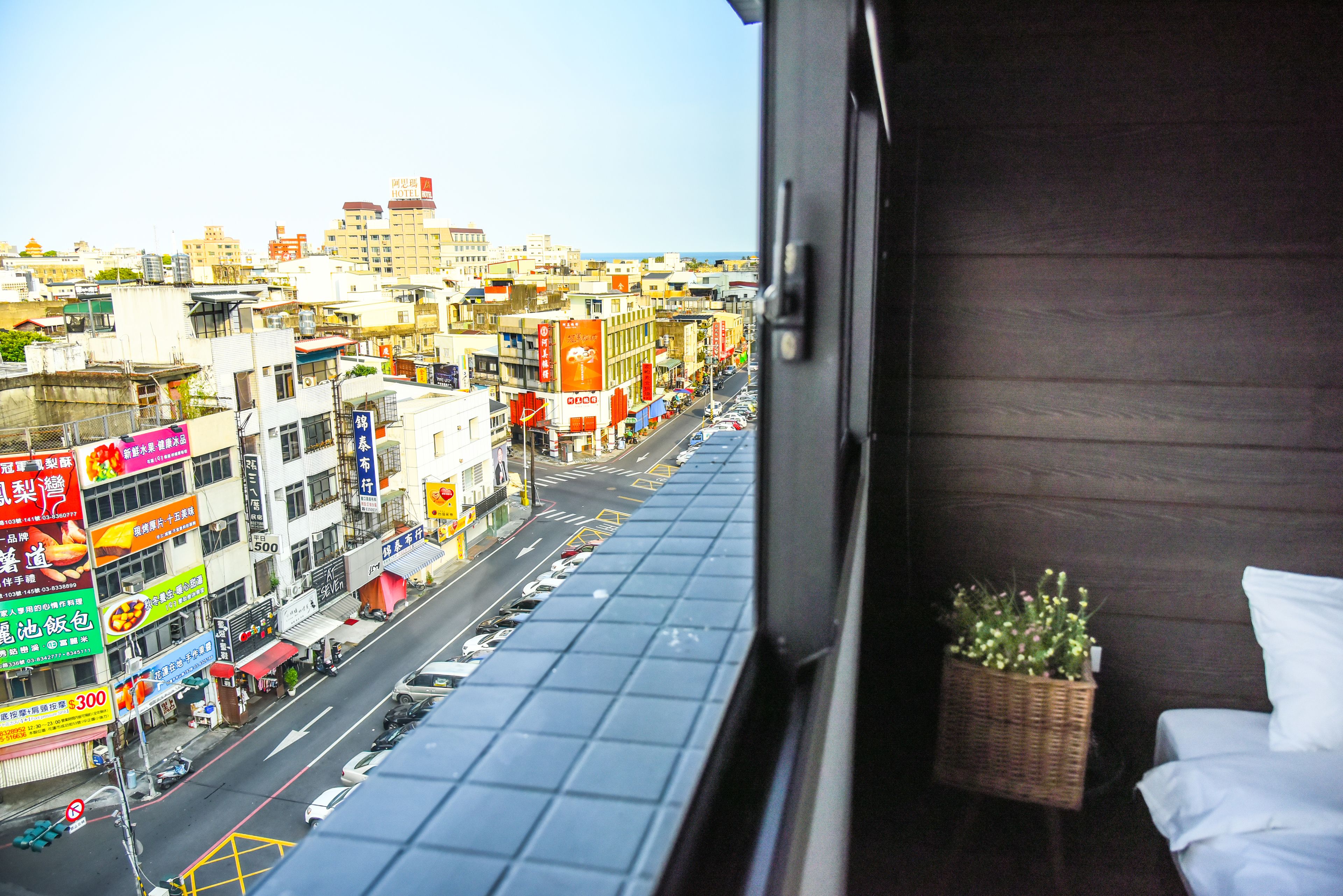 A city view from a balcony with a wicker basket of flowers and a white pillow.