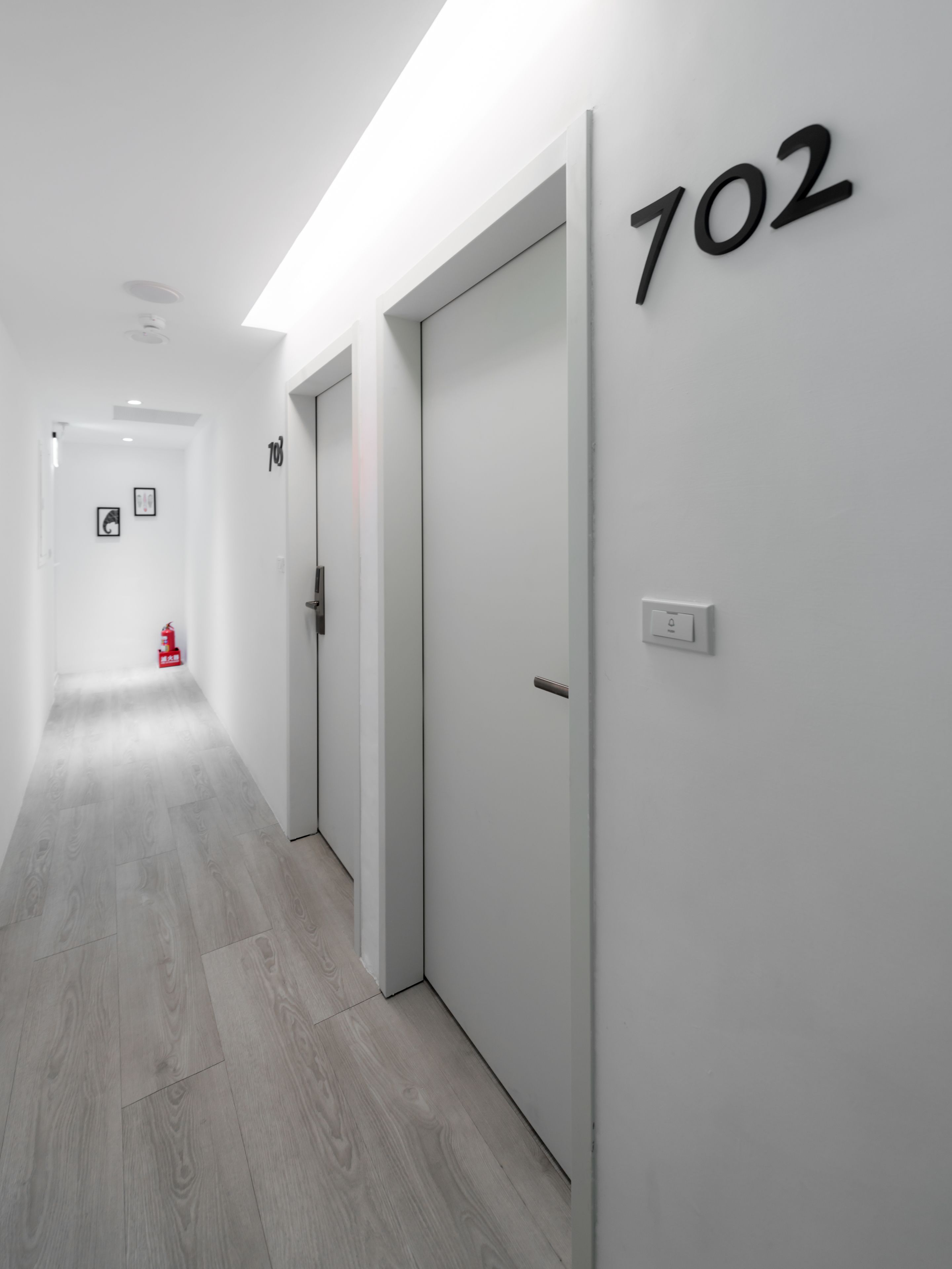A hallway with a wooden floor, white walls, and doors numbered 102.