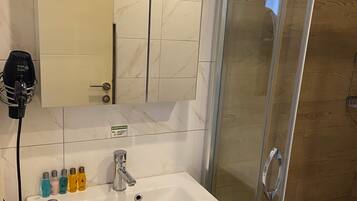 Une salle de bain avec un lavabo blanc, un miroir, une douche en verre et des articles de toilette posés sur le lavabo.