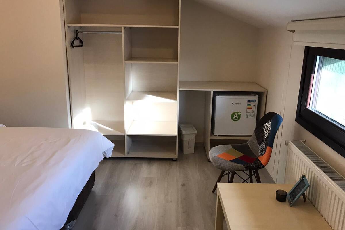A hotel room with a bed, a desk, a chair, a radiator, and a window.