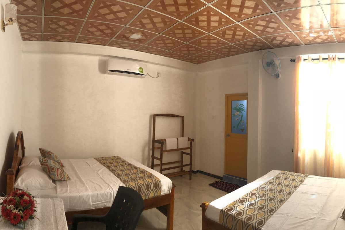 A room with two beds, a wooden ceiling, a fan, and a window with curtains.