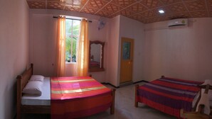 Una habitación con dos camas de madera, una ventana con cortinas, un ventilador, aire acondicionado y una puerta con un cuadro.