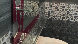 Un baño moderno con cabina de ducha de vidrio, un espejo grande y azulejos estampados.