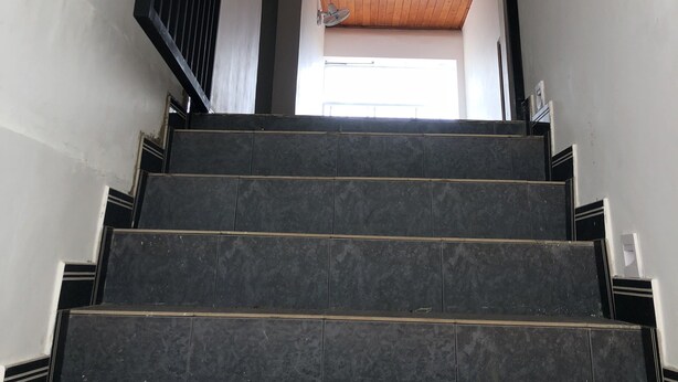 Una escalera con peldaños oscuros que conduce a una habitación con techo de madera y ventilador de techo.