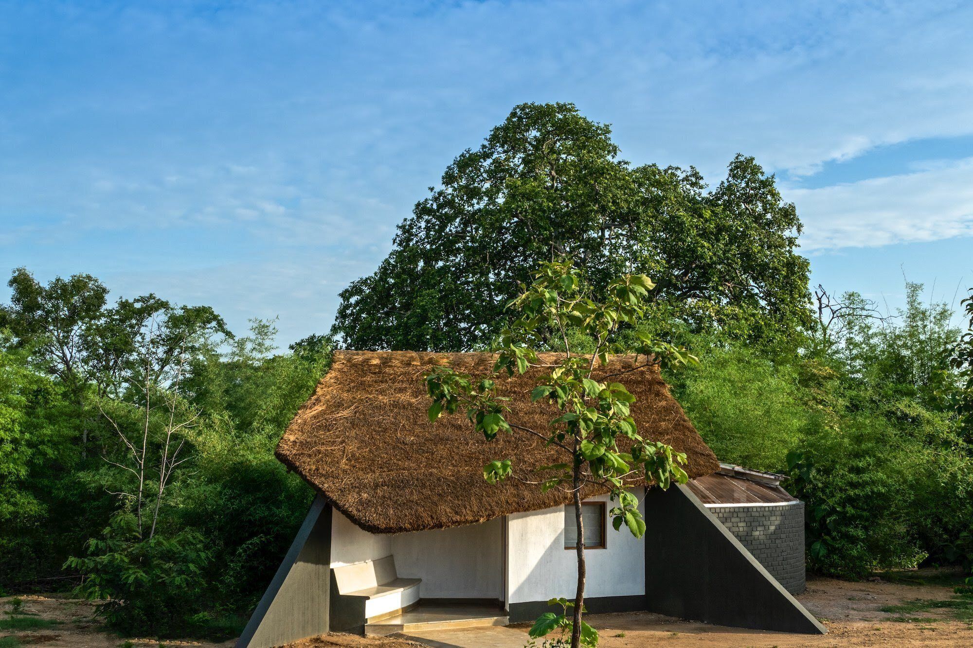 A small, thatched-roof structure with a sloped roof, surrounded by dense greenery.