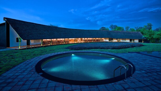 A modern building with a curved roof, a swimming pool, and a well-maintained lawn. - Red Earth Tadoba (Chandrapur)