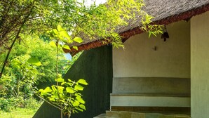 A building with a thatched roof, a staircase leading to an upper level, and a small tree in the foreground. - Red Earth Tadoba (Chandrapur)