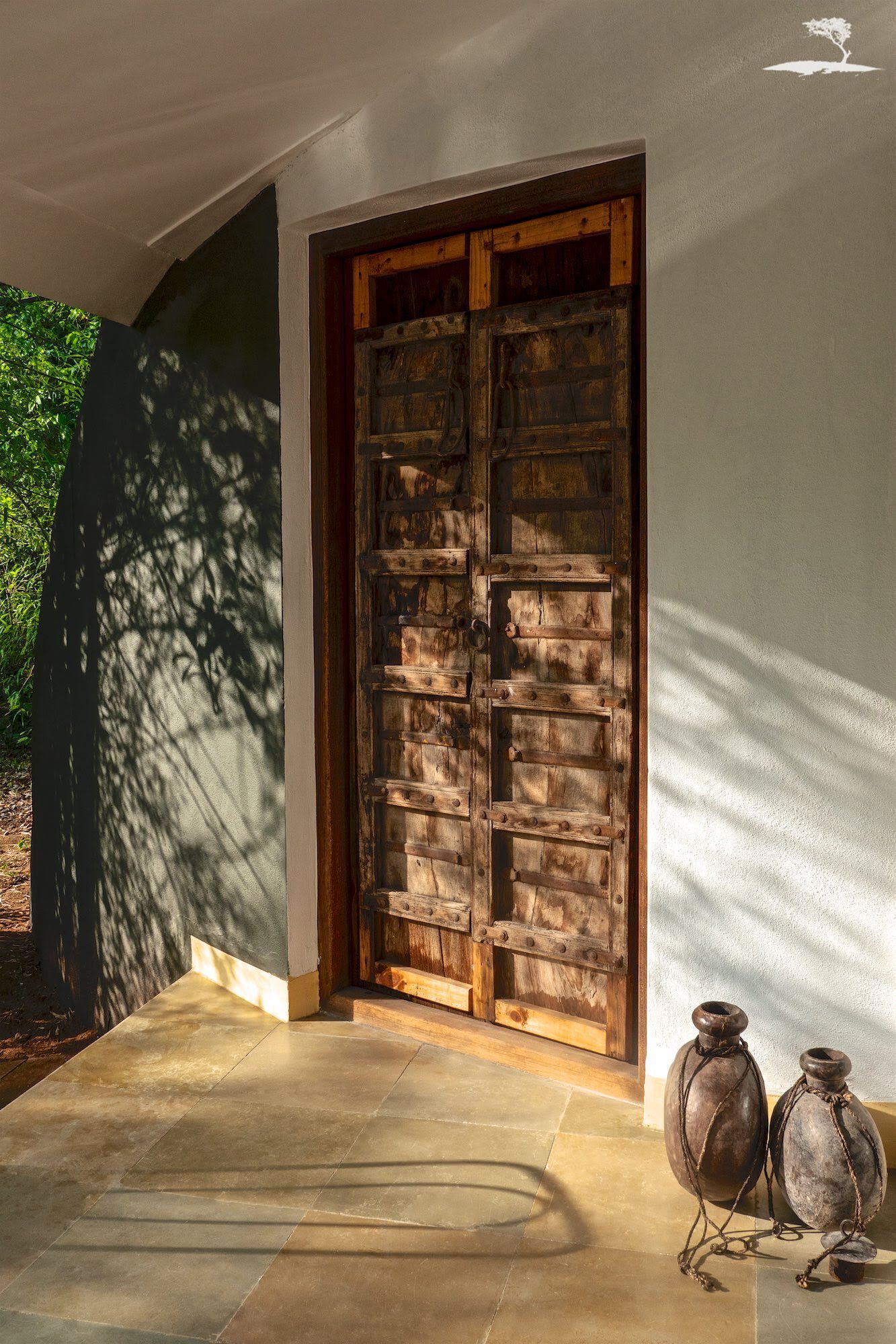 A rustic wooden door with a metal latch, a concrete pathway leading to it, and two ceramic pots on the right.