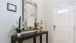 Une console en bois foncé, agrémentée d’un miroir et de deux vases décoratifs, un certificat encadré accroché au mur, et une porte blanche avec une petite fenêtre.
