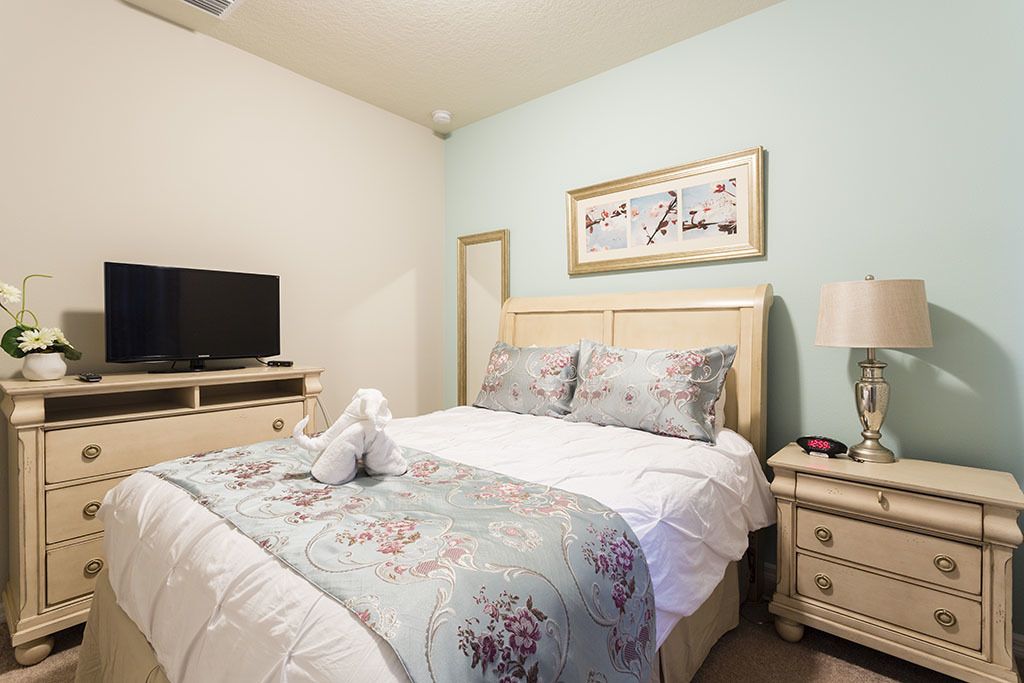 A bedroom with a bed, a television, a nightstand, a lamp, and a framed picture on the wall.