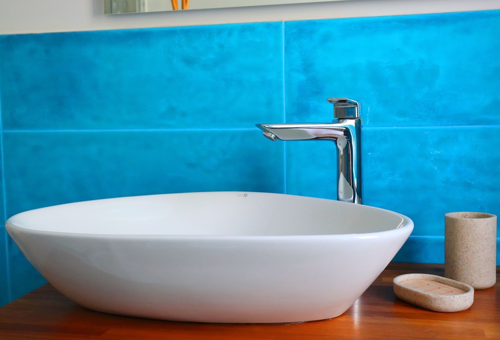 A white ceramic sink with a modern faucet, set against a blue tiled wall.