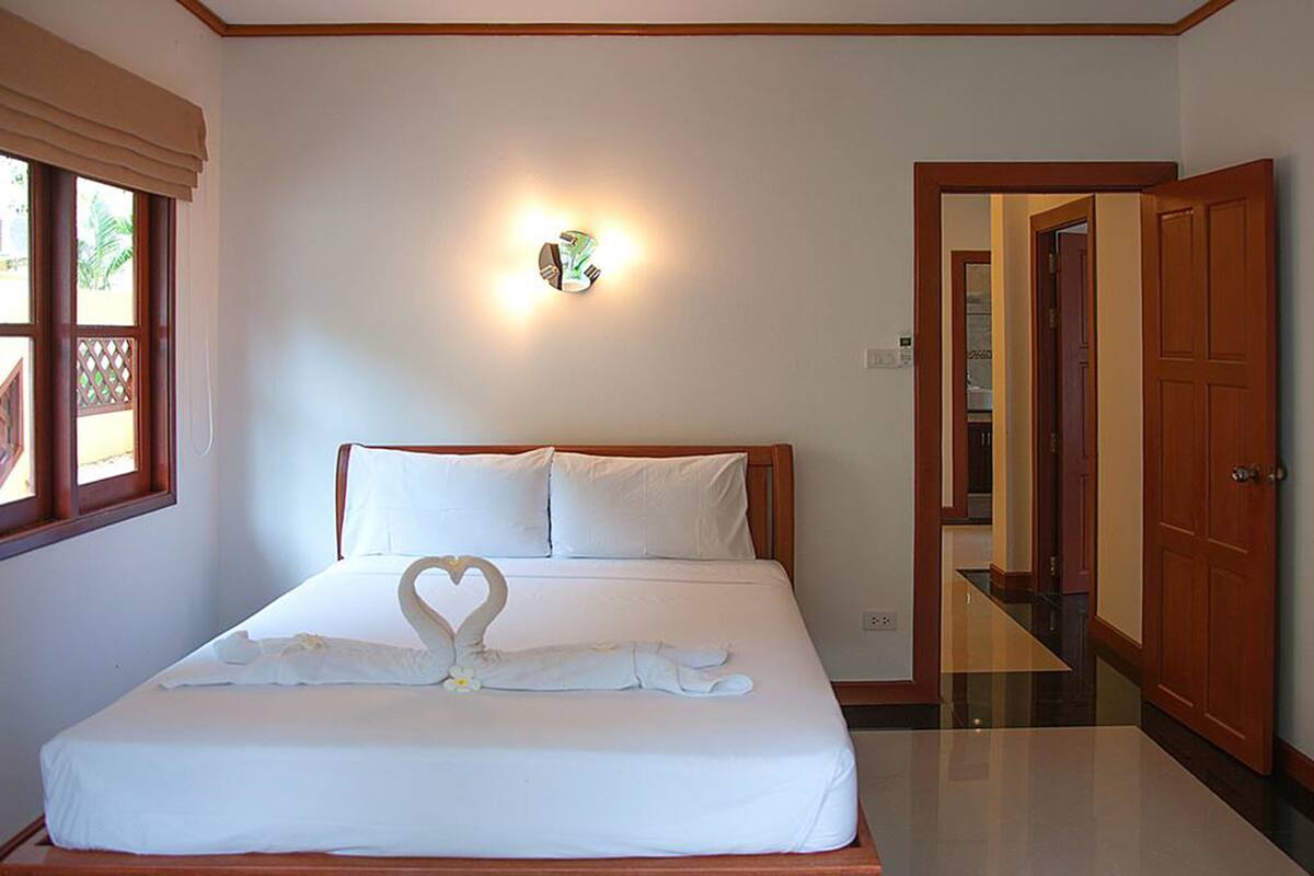 A neatly made bed with white linens and a heart-shaped towel arrangement.