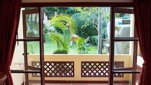 Une chambre d’hôtel avec un lit, une table en bois et une vue sur un jardin, visible à travers une porte-fenêtre coulissante.