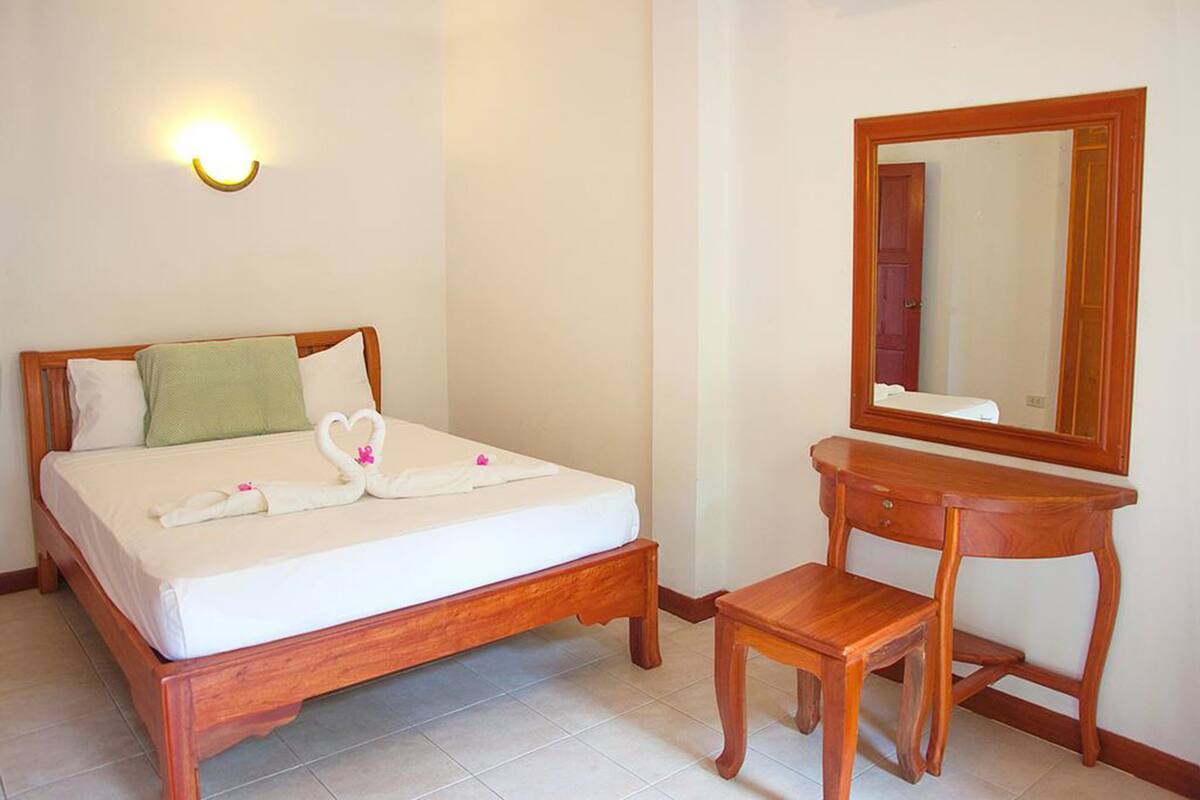 A neatly made bed with a wooden headboard, a bedside table with a mirror, and a small wooden stool.
