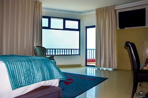 A hotel room with a bed, a chair, a TV, and a large window.