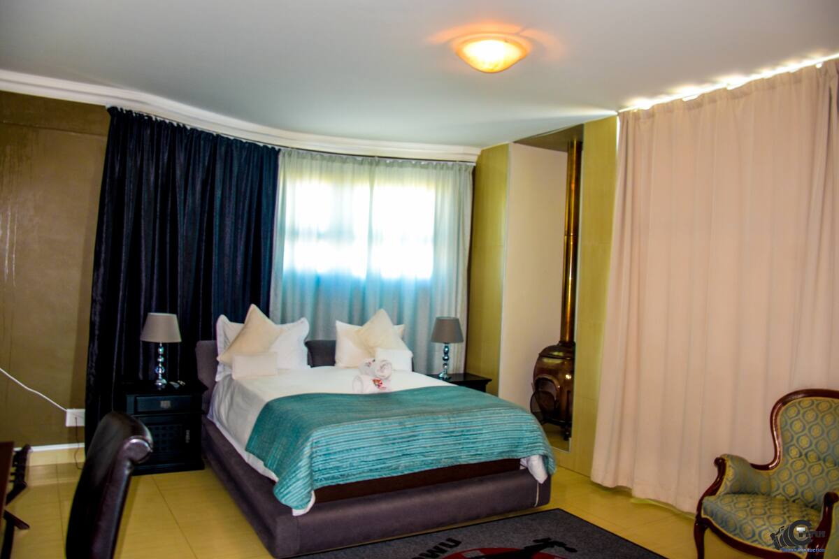 Una habitación de hotel con cama, mesitas de noche, una silla y ventana con cortinas.