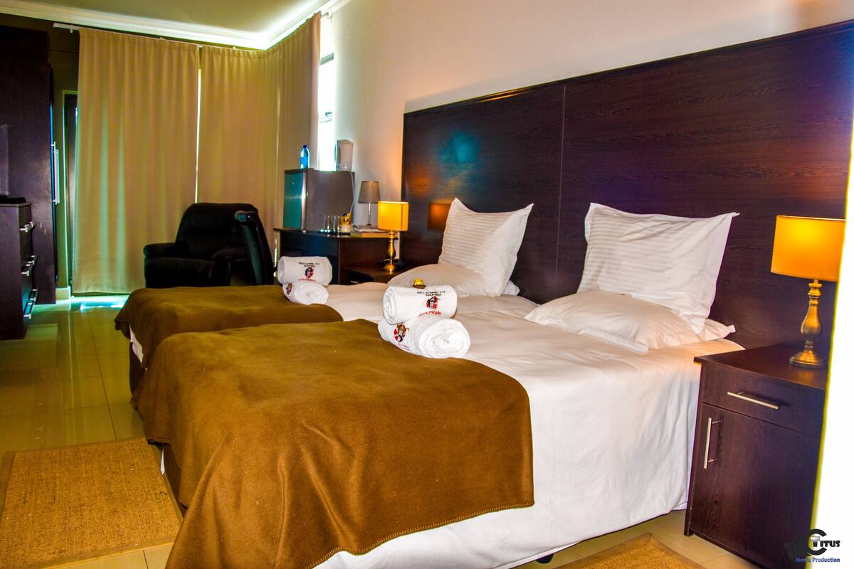 Una habitación de hotel con dos camas, un escritorio, una silla, una lámpara y una mesita de noche.