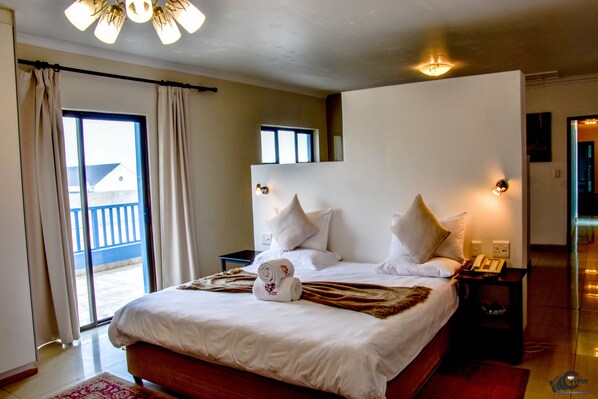 A hotel room with a large bed, a nightstand, a telephone, and a view of the outside balcony.