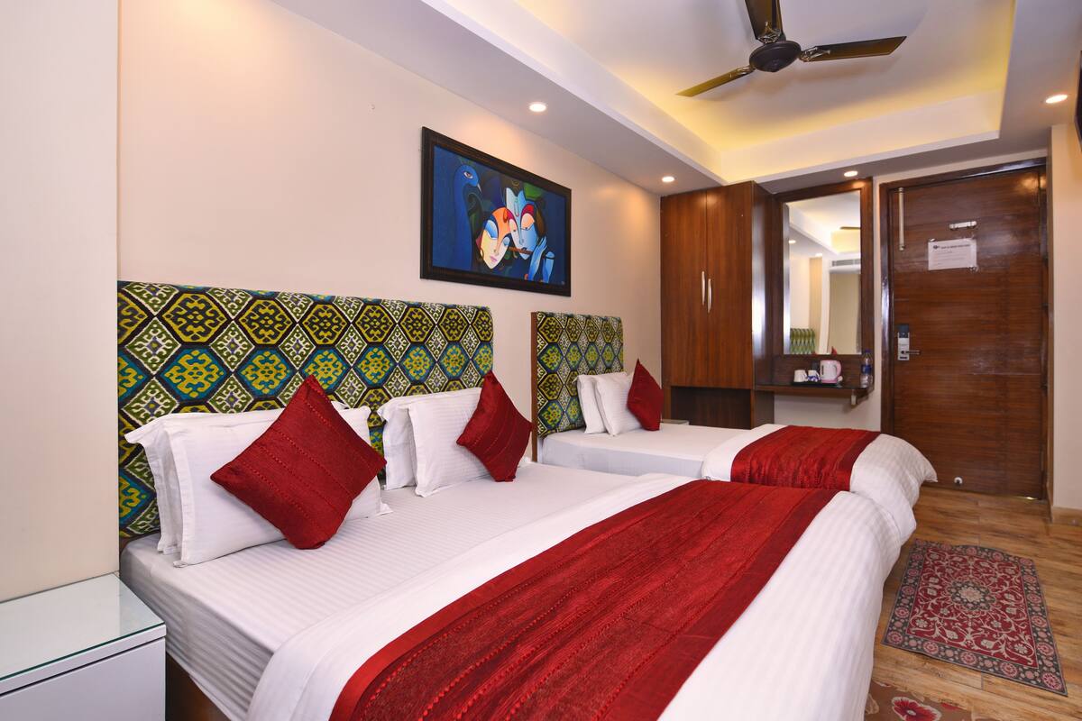 A hotel room with two beds, a ceiling fan, a painting on the wall, and a wooden door.