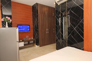 A hotel room with a bed, a TV, a wooden wardrobe, a marble-patterned wall, and a small table with a vase of flowers.