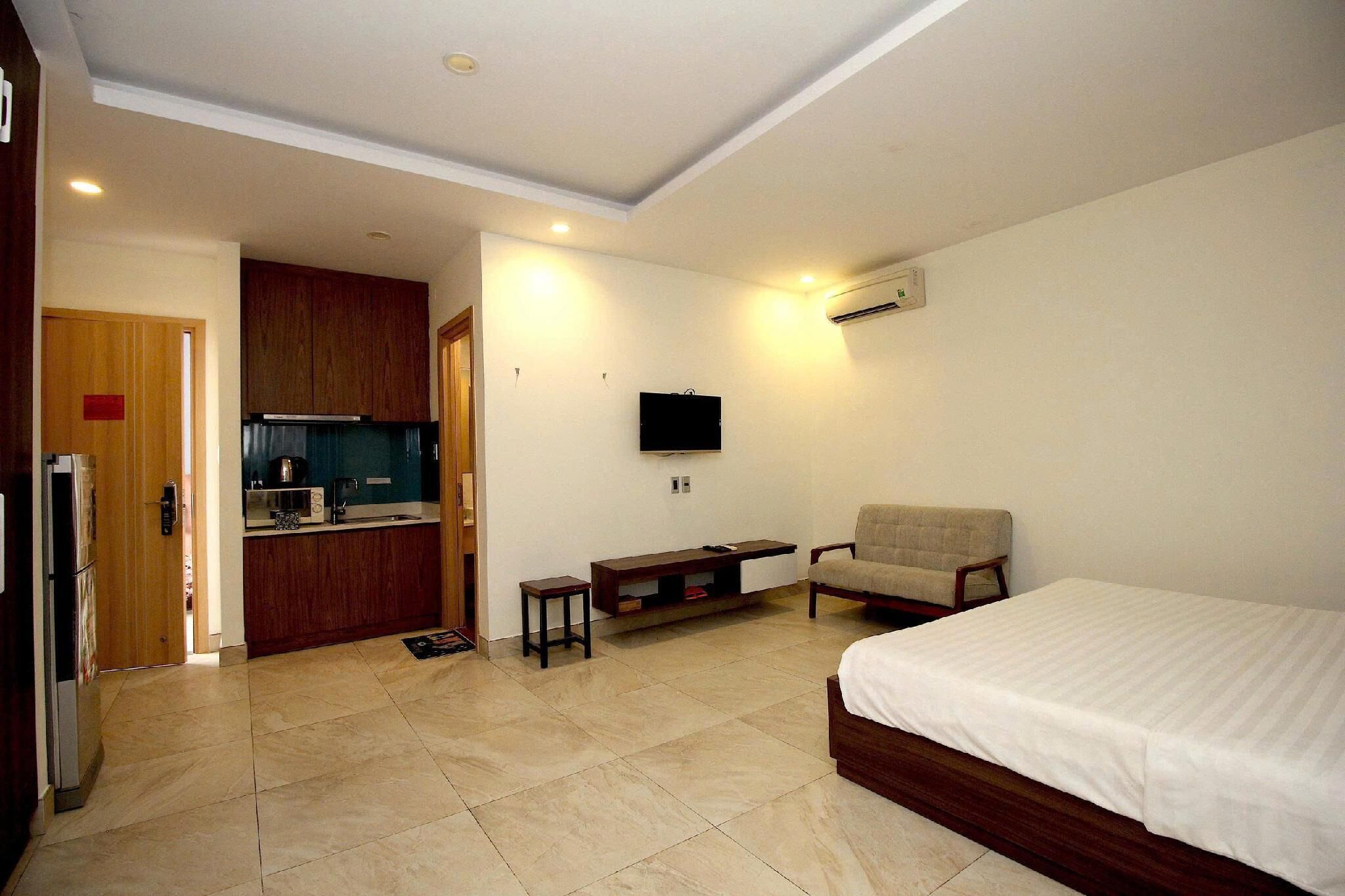 A room with a bed, a chair, a TV, a kitchenette, and an air conditioning unit.