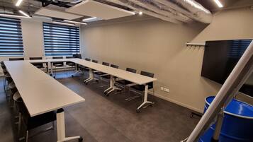 Une salle de conférence avec une longue table, des chaises, un grand écran et une poubelle bleue.